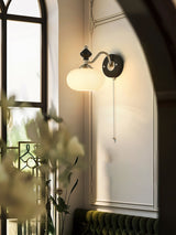 Lamp lit beside a mirror reflecting a green wall and a vase of flowers