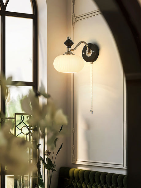 Lamp lit beside a mirror reflecting a green wall and a vase of flowers