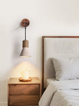 The cone light above a walnut nightstand with a cup, beside a pillow