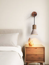 The travertine cone hanging above a wood nightstand with a lamp beside a bed