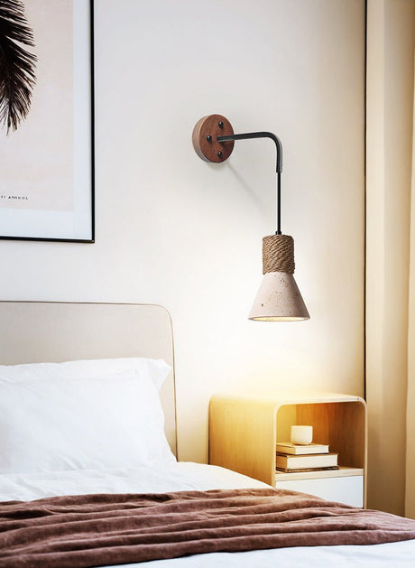 The cone light lit above a small wood nightstand beside a bed and a throw