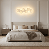 A horizontal row of glowing ceramic discs above an upholstered bed and two nightstands