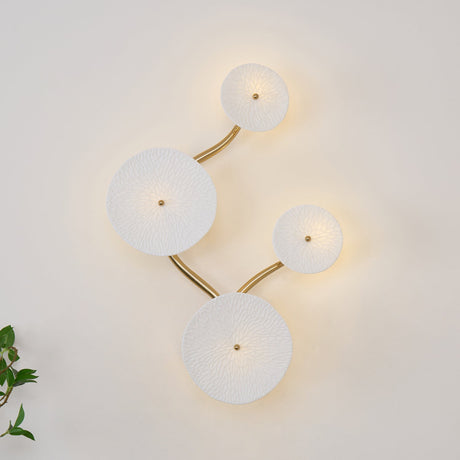 Four discs unlit on a white wall, the gold stem curving between them