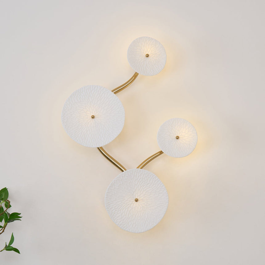 Four discs unlit on a white wall, the gold stem curving between them