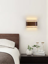 Sconce lit above a dark nightstand with two clear vases beside a bed