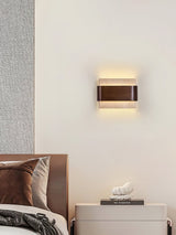 Sconce lit beside a wood headboard above a pale bedside cabinet