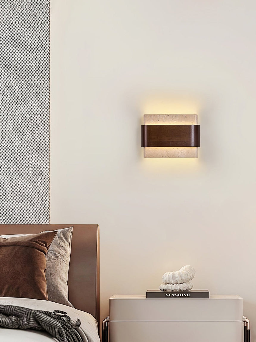 Sconce lit beside a wood headboard above a pale bedside cabinet