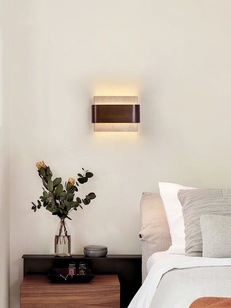 Sconce lit beside a bed above a nightstand holding a small green plant
