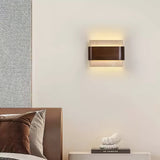 Sconce lit above a bed with rust cushions and a book on the nightstand