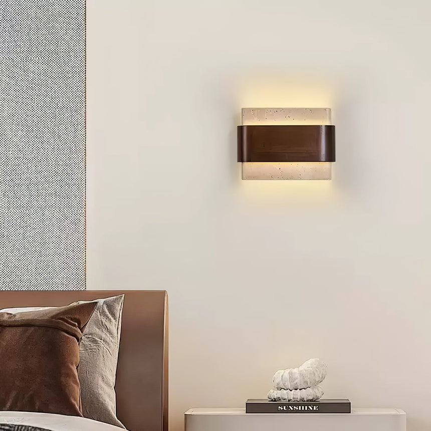 Sconce lit above a bed with rust cushions and a book on the nightstand