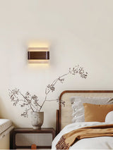 Sconce lit above a bed beside dried branches in a tall stone vase