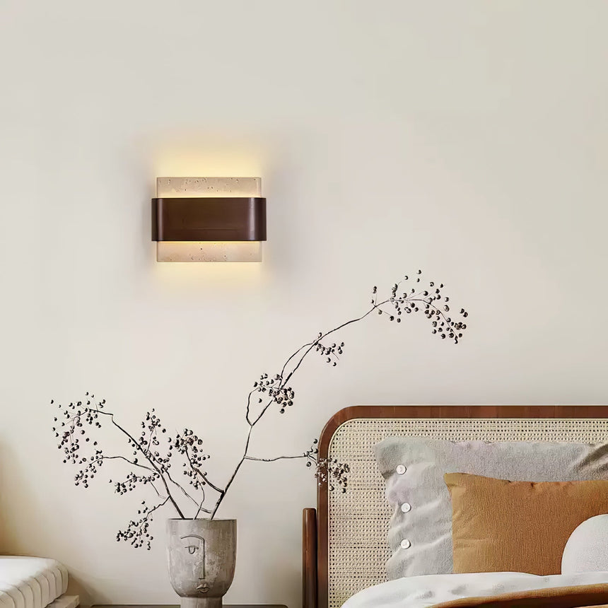 Sconce lit above a bed with ochre cushions and a woven headboard