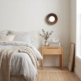 Sconce unlit above a bed with a nightstand, a vase and framed prints leaning