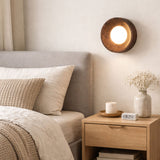 Sconce lit above a bed beside a wood nightstand holding a candle and a book
