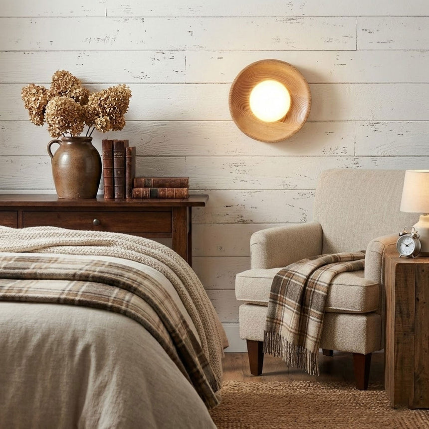 Sconce lit on a brick wall above a dresser with dried flowers in a jug
