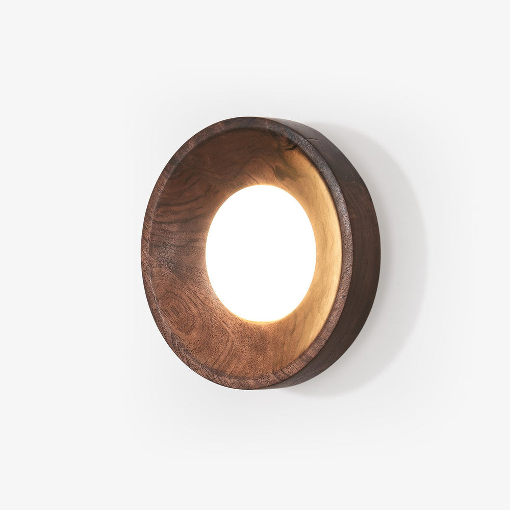 Wall sconce above a bed, a straight sided wood drum with a lit white disc
