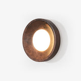 Wall sconce above a bed, a straight sided wood drum with a lit white disc