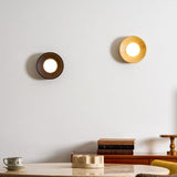 Two sconces on a wall above a desk with books, one walnut and one light wood