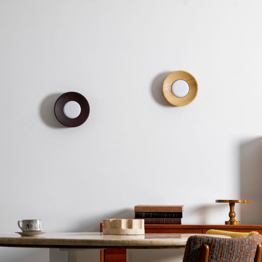 Two sconces lit above a desk holding a cup and books, walnut beside light wood