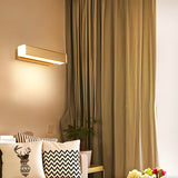 Sconce lit beside a long curtain above a sofa with patterned cushions