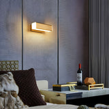 Sconce lit above a sofa with a dark cushion beside a low table and a bottle