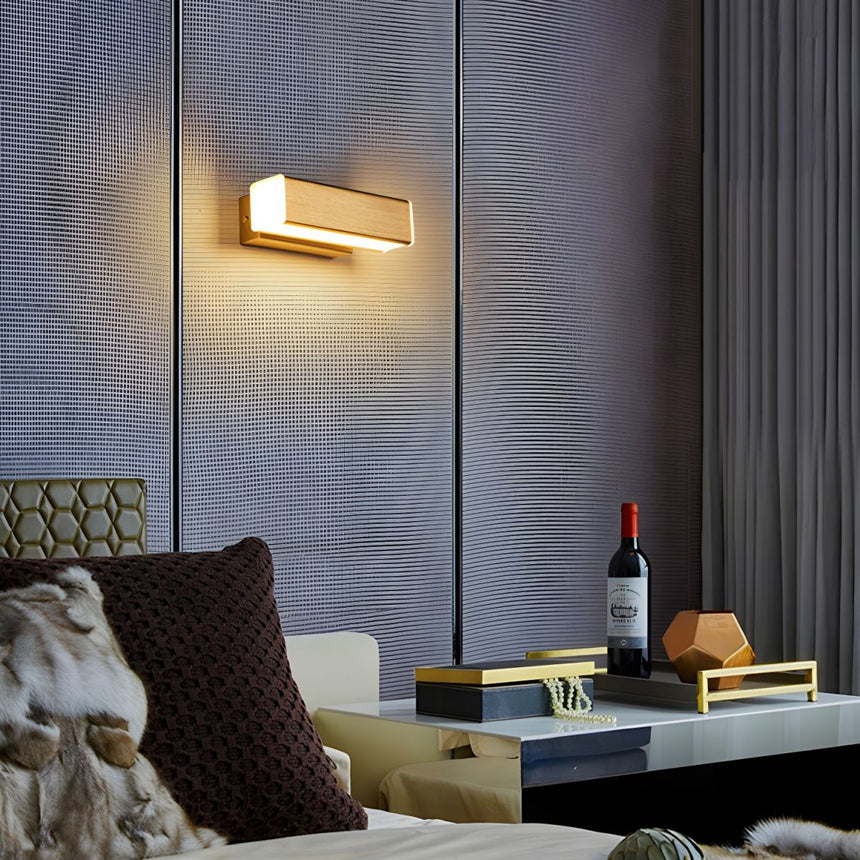 Sconce lit above a sofa with a dark cushion beside a low table and a bottle