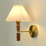 Pleated shade lit, seen from the side with the brass arm and wall plate
