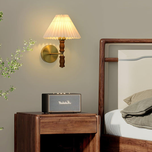 Pleated wall sconce lit beside a cane headboard and a wood nightstand