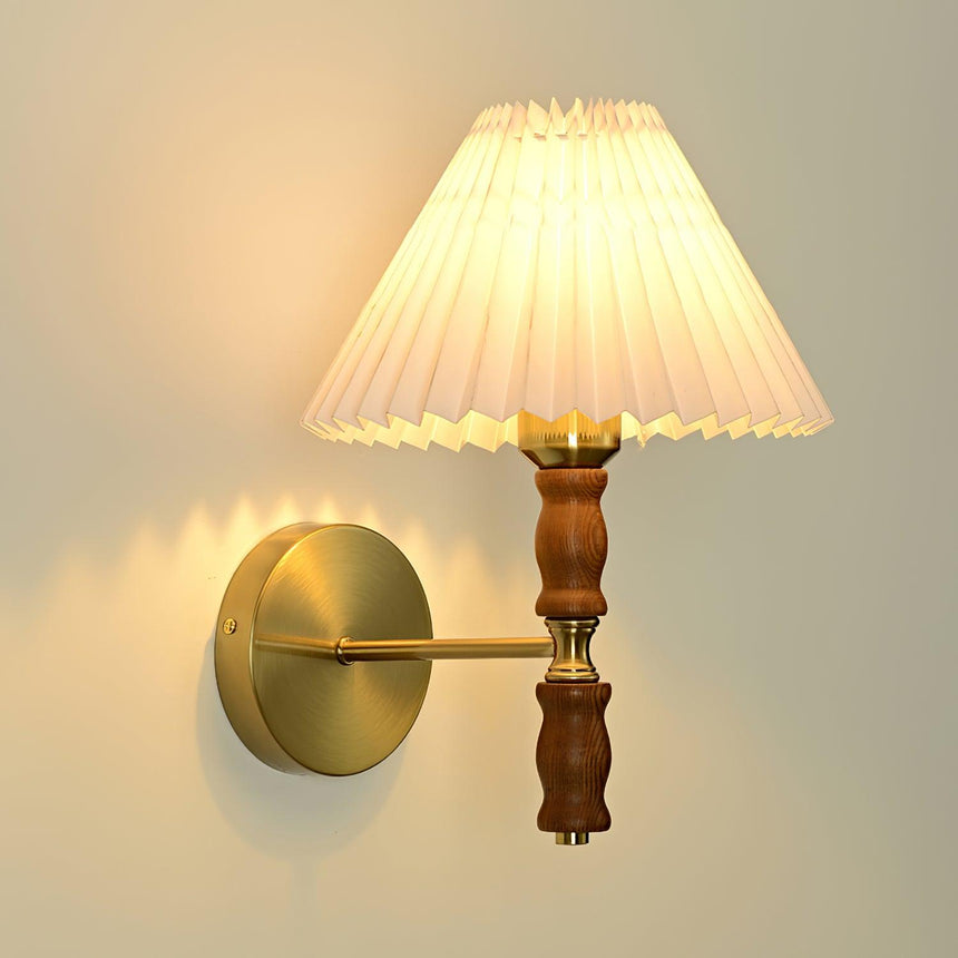 Pleated fabric shade lit straight on above a brass arm and walnut turning
