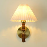 Pleated white shade lit above a turned walnut column and brass arm