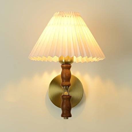 Pleated white shade lit above a turned walnut column and brass arm