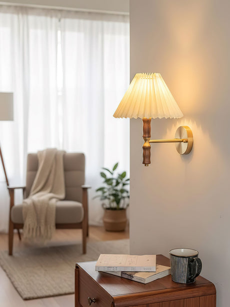 Pleated wall sconce lit beside an armchair with a throw over the arm