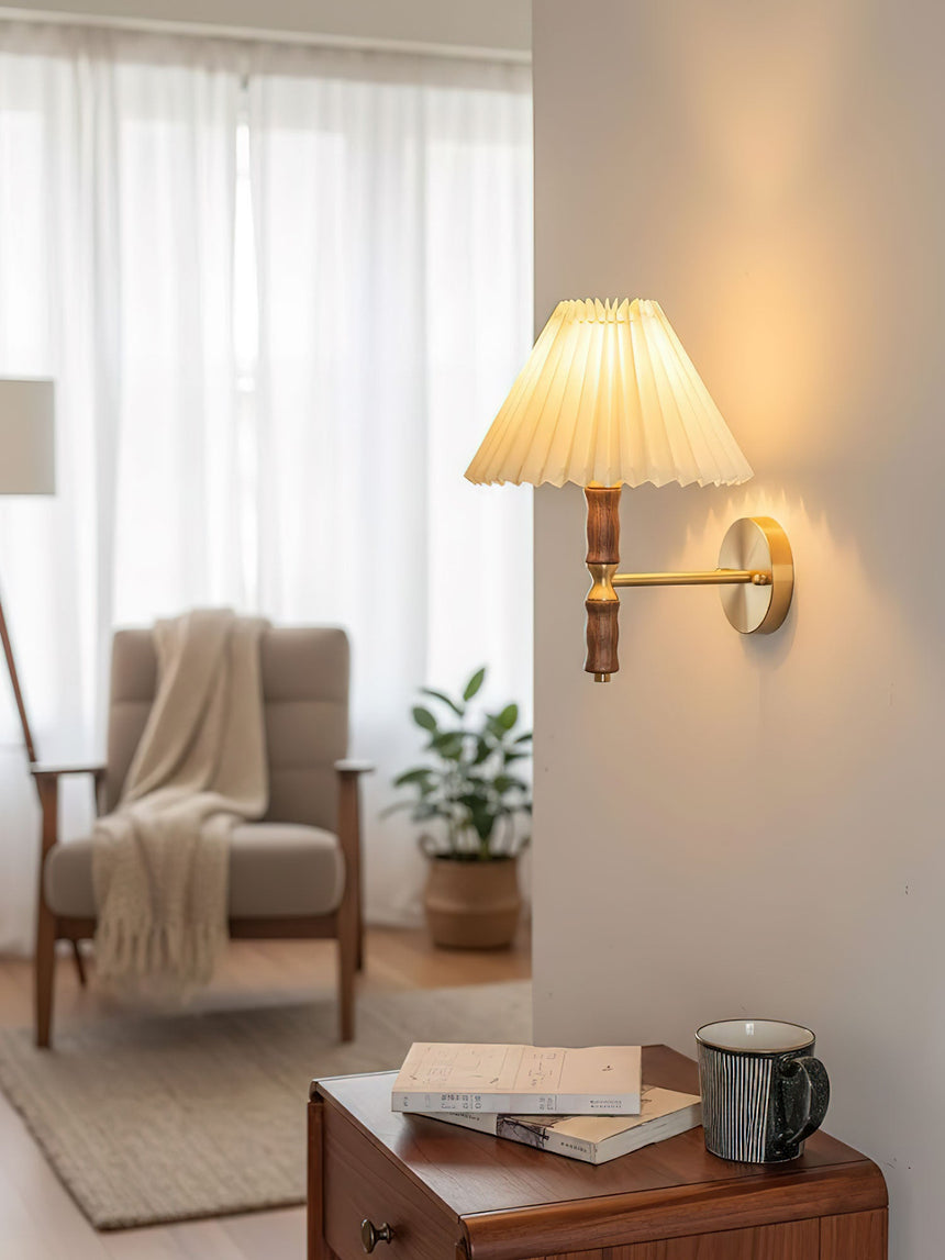 Pleated wall sconce lit beside an armchair with a throw over the arm