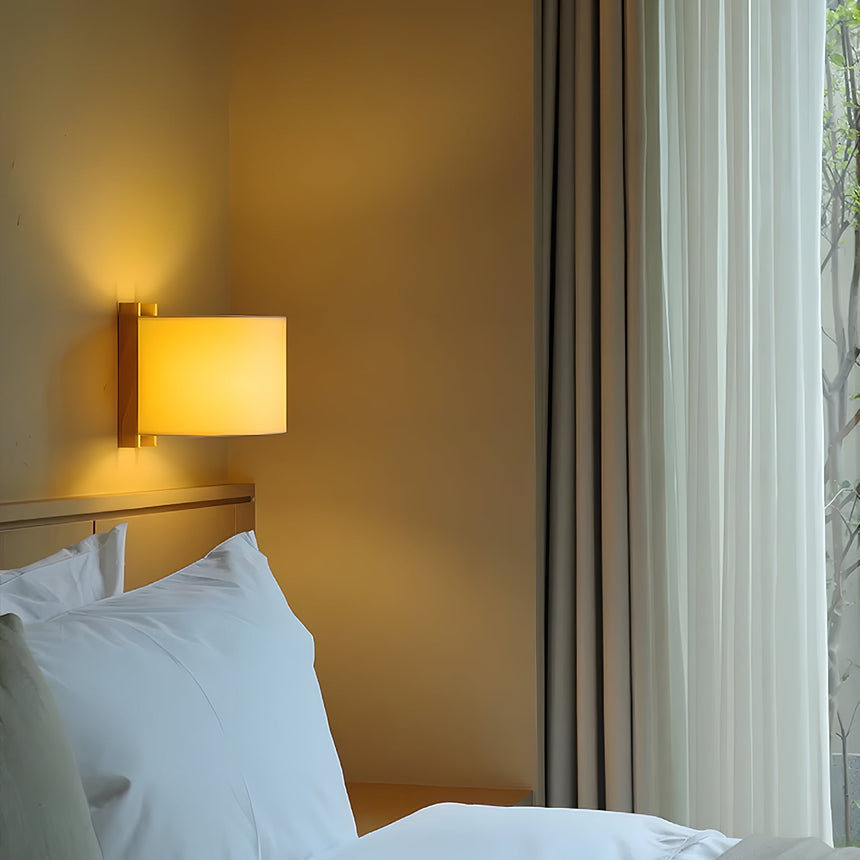Sconce lit above a bed with white pillows, a window and a sheer curtain