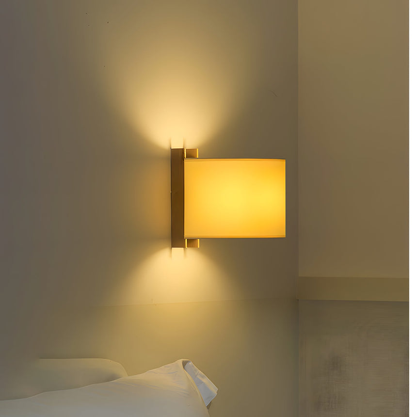 Sconce lit above a bed, light spilling up the wall and down on the pillow