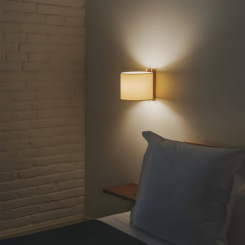 Sconce lit on a brick wall above a bed with a dark bolster cushion