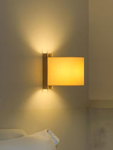 Sconce lit above a bed, the beige shade glowing against a warm plaster wall