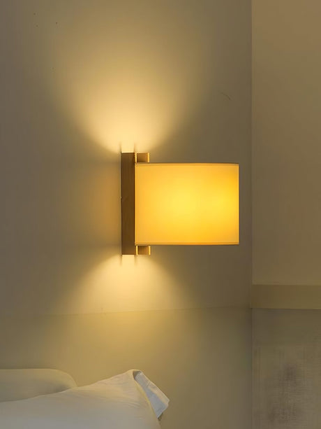 Sconce lit above a bed, the beige shade glowing against a warm plaster wall