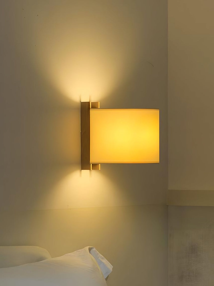 Sconce lit above a bed, the beige shade glowing against a warm plaster wall