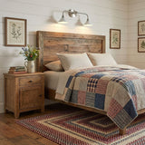 A double sconce above a reclaimed wood headboard and a patchwork quilt