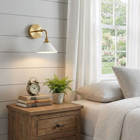 The single sconce above a wood nightstand with an alarm clock and a small plant