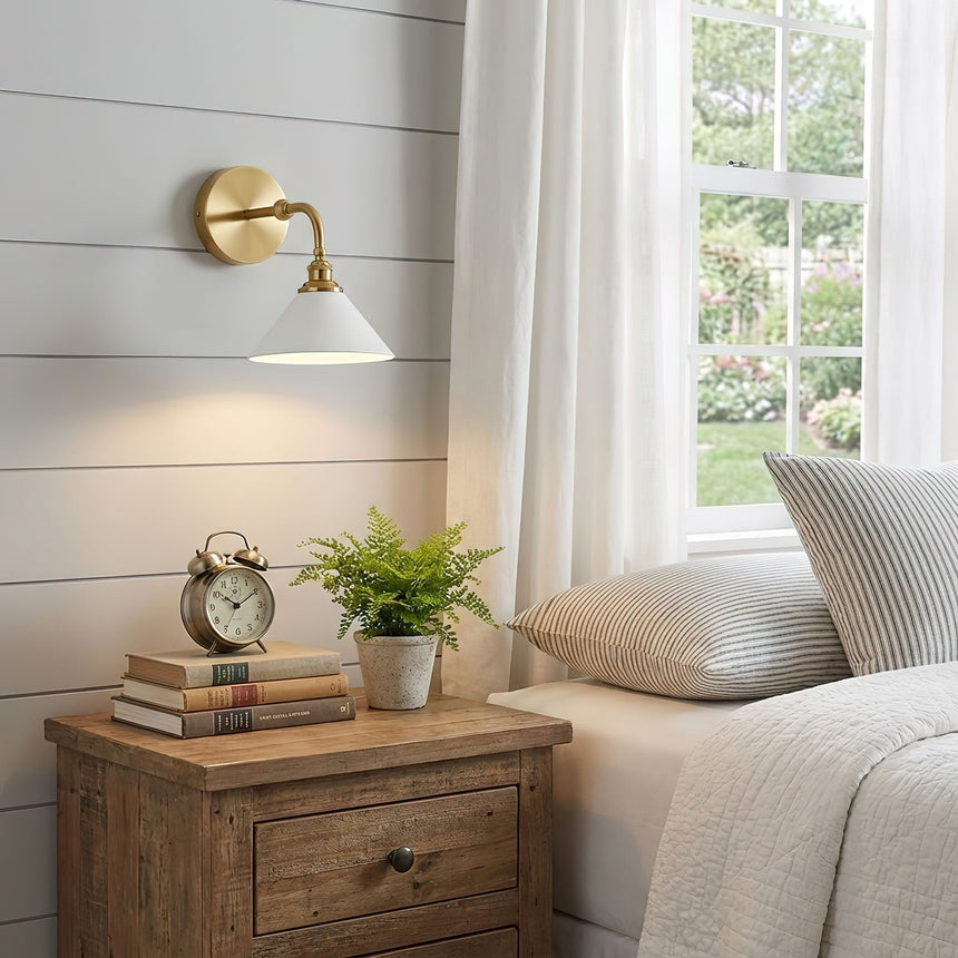The single sconce above a wood nightstand with an alarm clock and a small plant