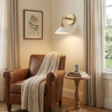 The sconce lit above a leather armchair and a small side table in a reading corner