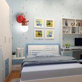 The tiger lamp lit on the wall of a kids bedroom beside framed pictures and a bed