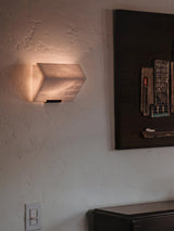 A single alabaster block lit on a textured wall beside a dark framed artwork