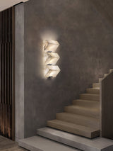 The stepped alabaster sconce lit on a concrete wall above a flight of pale steps