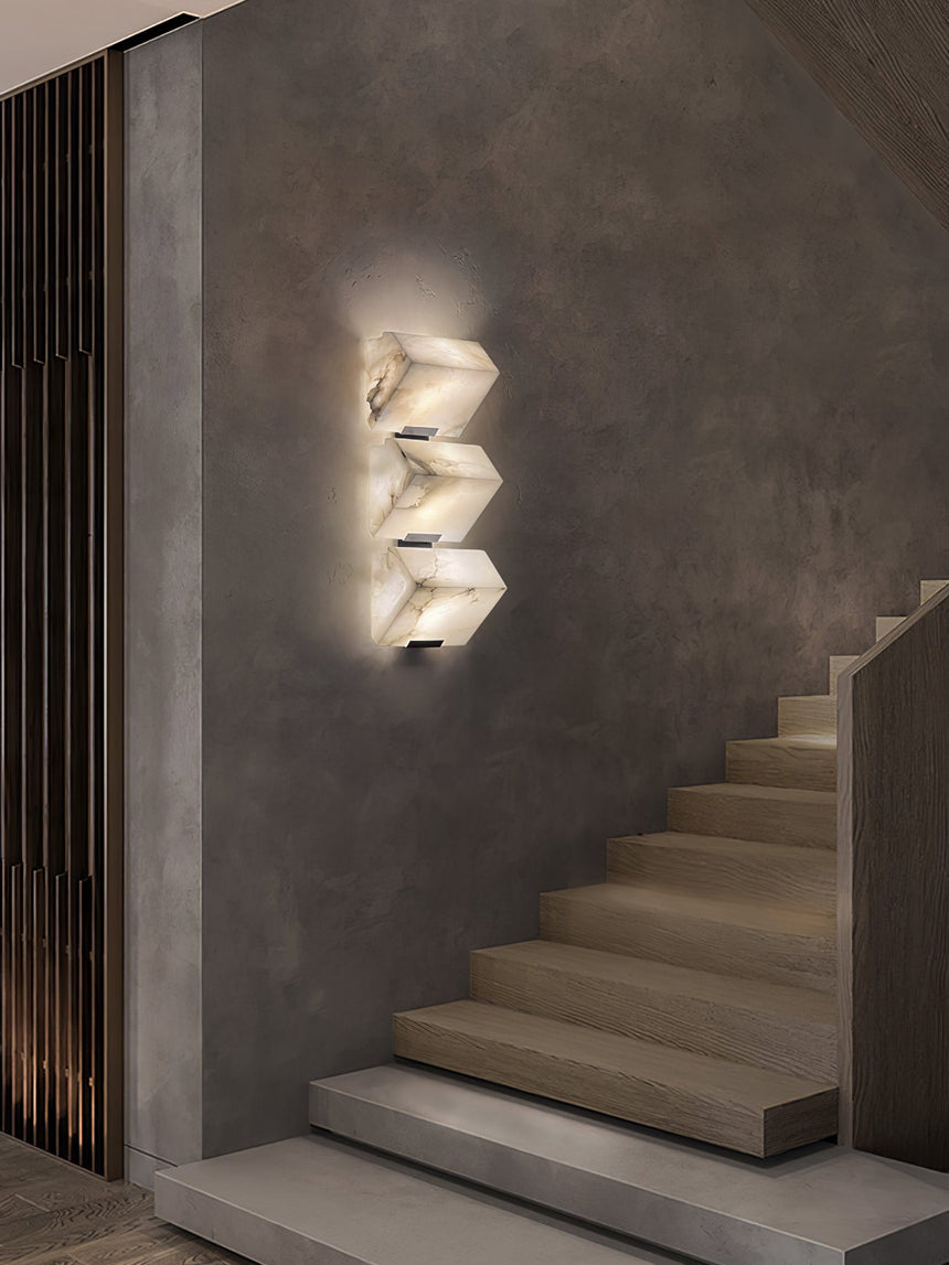 The stepped alabaster sconce lit on a concrete wall above a flight of pale steps