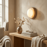 Sconce lit above a wood console with dried grasses, books and a folded throw
