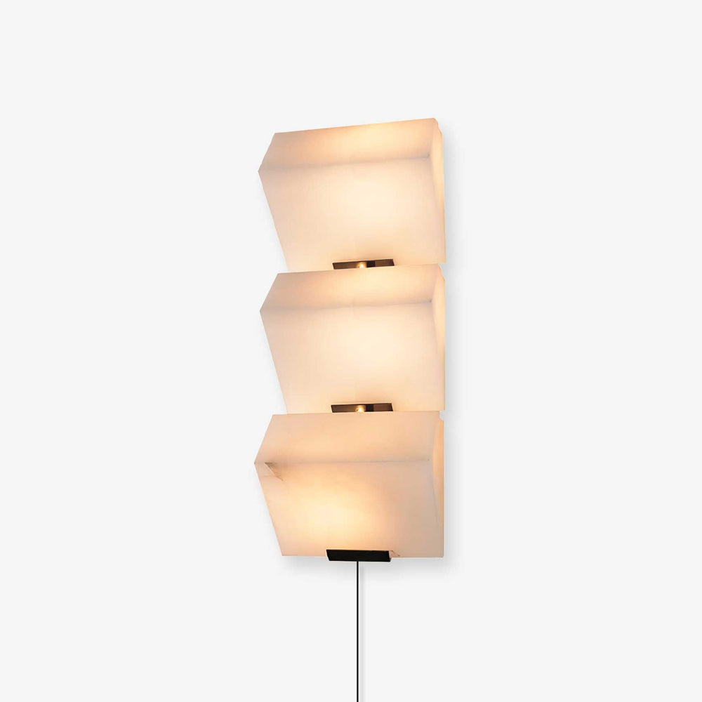 Plug-in wall lamp of three stepped alabaster blocks, lit, the cord running down