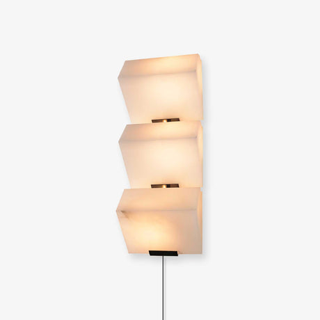 Plug-in wall lamp of three stepped alabaster blocks, lit, the cord running down